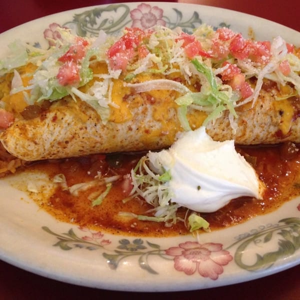 A large, cheesy Jalisco's Mexican Restaurant burrito topped with lettuce, tomatoes, and sour cream.
